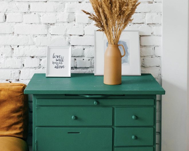 A cozy room with a green dresser and dried flowers in a vase